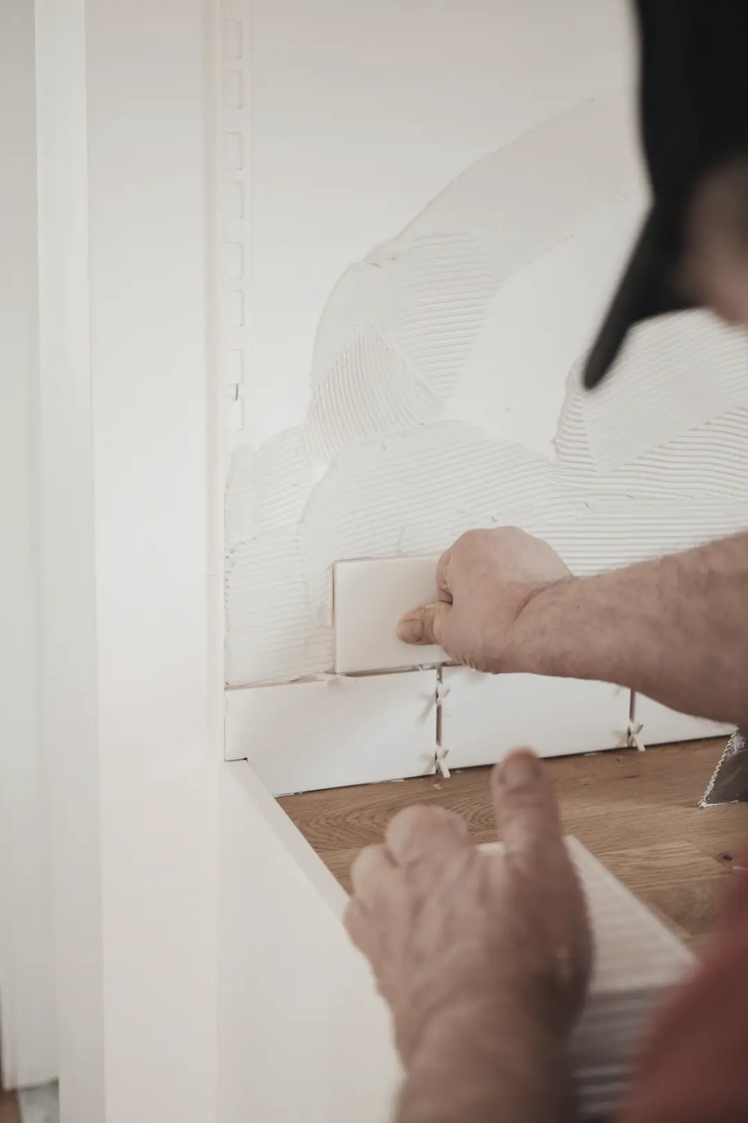 Main qui pose un carreau blanc sur un mur, avec ses croisillons