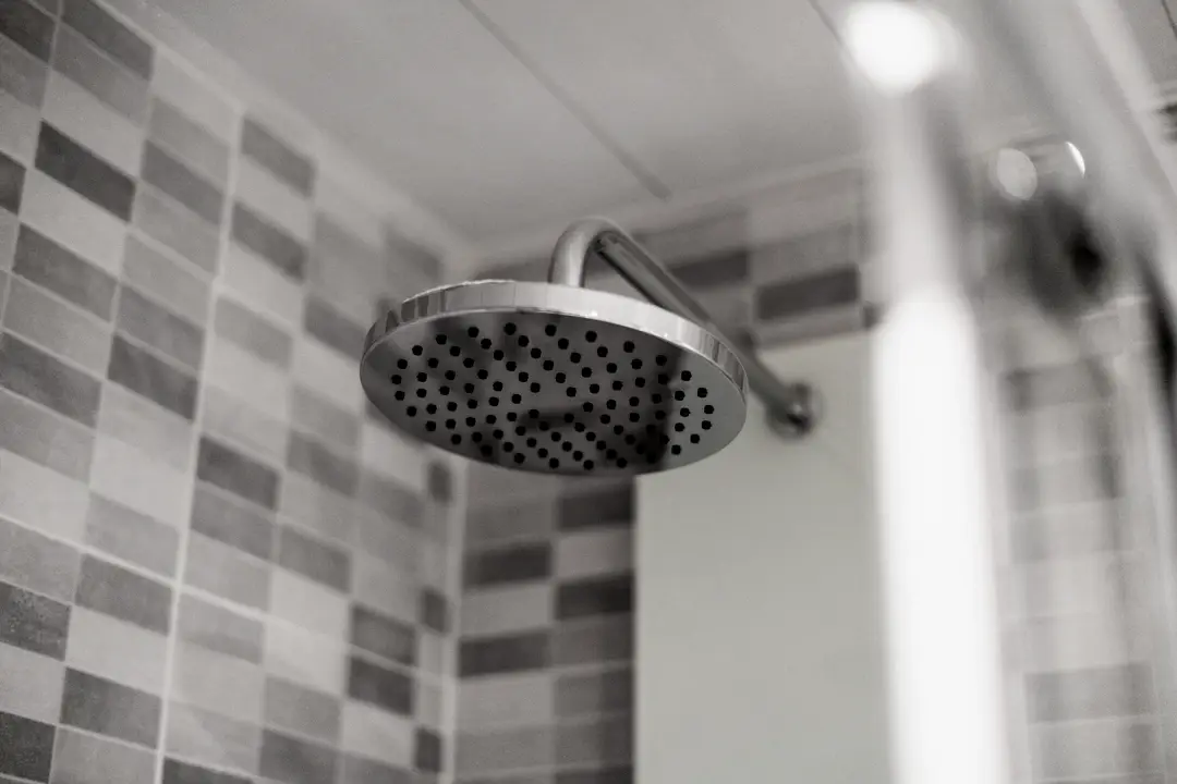 Pomme de douche en acier devant un mur de céramique rectangulaire grise