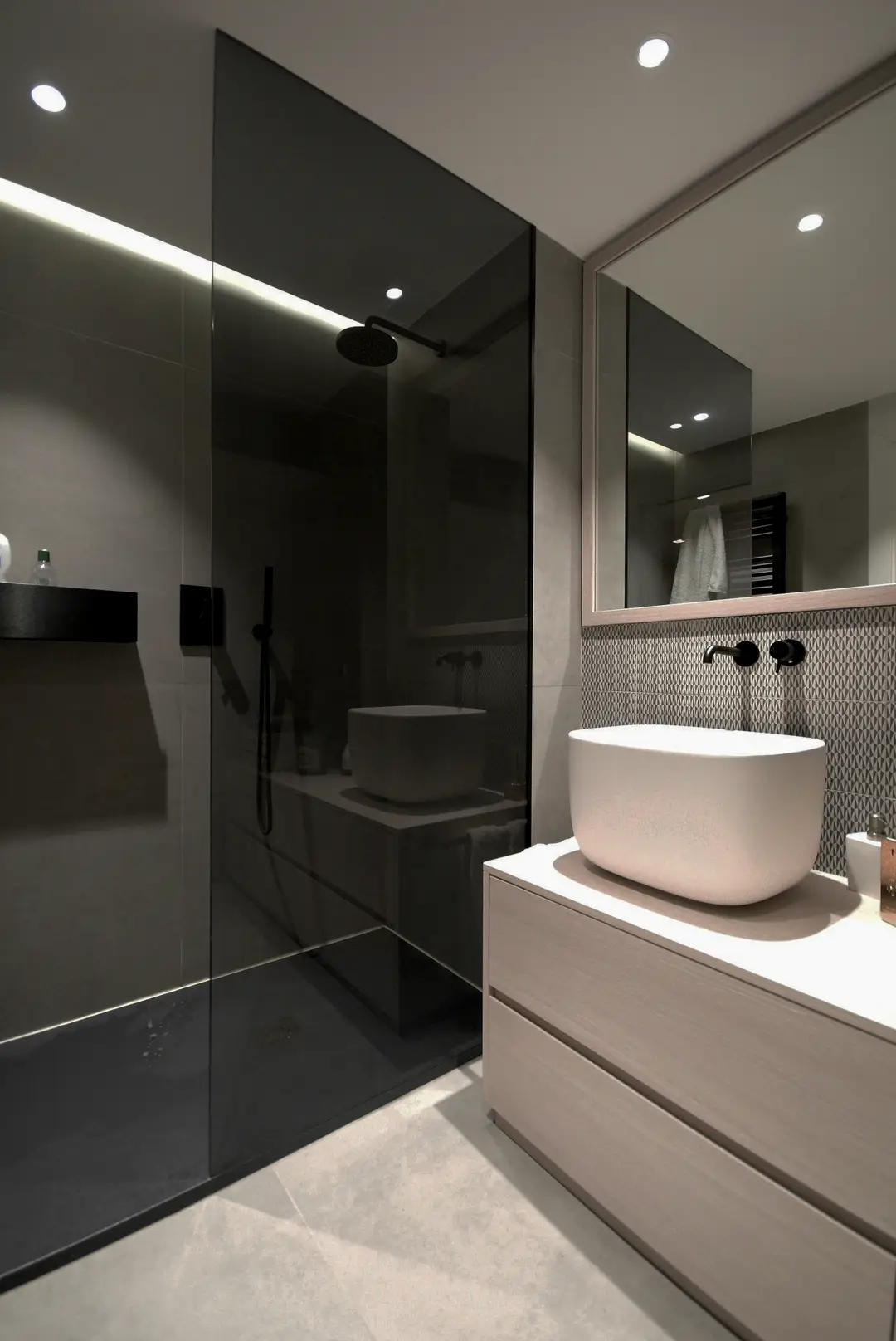 Salle de bain aux tons sombres : vasque blanche posée, robinet mural noir et douche vitrée
