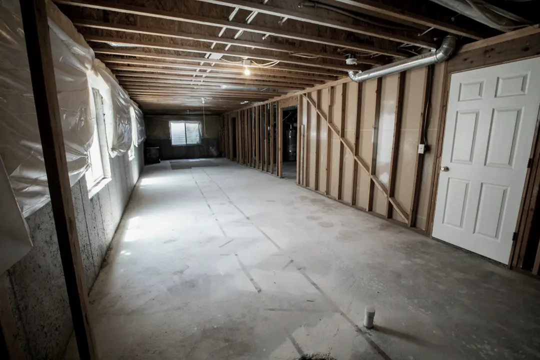 Sous-sol brut : solives apparentes, murs ouverts et plancher de béton
