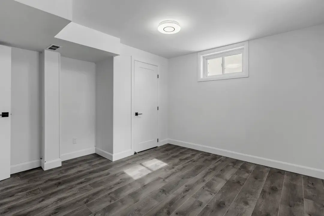 Sous-sol fini aux murs blancs, éclairage encastré et plancher de bois